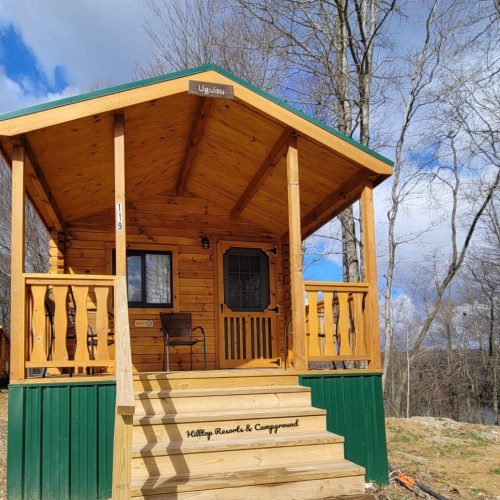A cozy wooden cabin with a porch, surrounded by trees and a blue sky at Killings Resort & Campground.