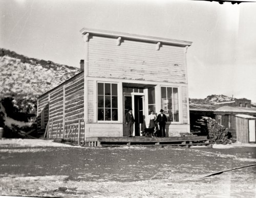 A historic wooden building with large windows, featuring four people standing at the entrance.