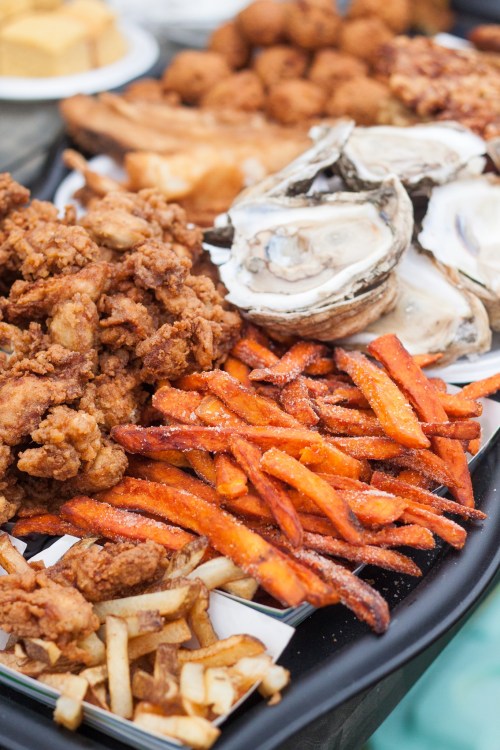 A platter featuring fried chicken, sweet potato fries, regular fries, and oysters.