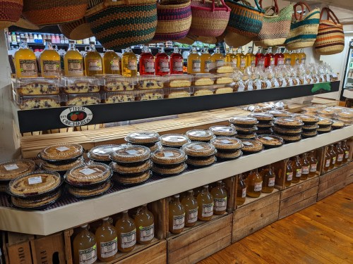 A display of pies, cakes, and beverages on shelves, with woven baskets hanging above in a cozy shop setting.