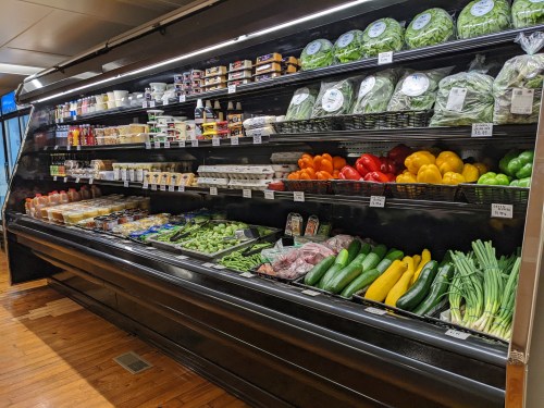 A grocery store display featuring a variety of fresh vegetables, fruits, and packaged goods on shelves.