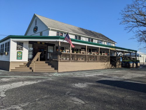 A two-story building with a green roof, wooden deck, and American flag, set against a clear blue sky.