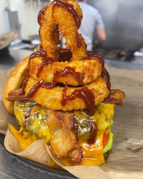 A towering burger topped with crispy onion rings, bacon, cheese, and drizzled with barbecue sauce on a bun.