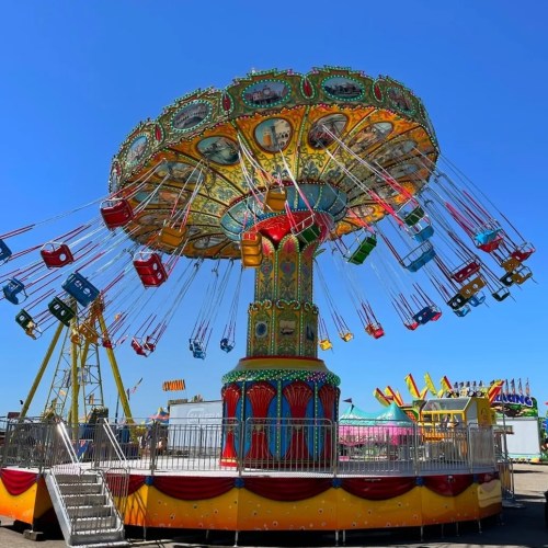 A colorful swing ride at a fair, with seats suspended from a central tower against a clear blue sky.