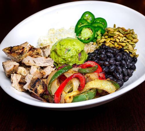 A bowl filled with grilled chicken, black beans, rice, guacamole, sautéed peppers, jalapeños, and pumpkin seeds.
