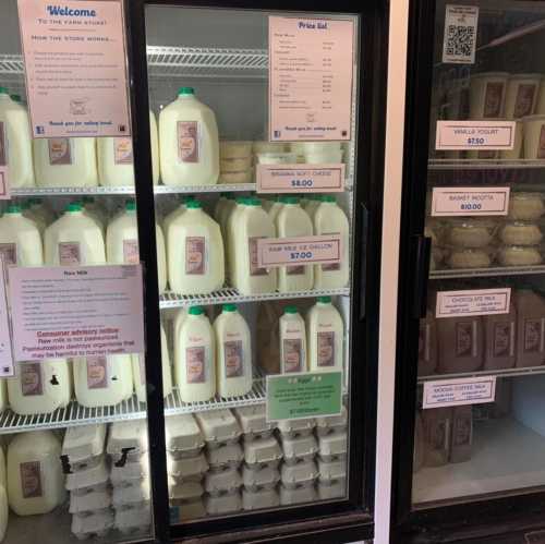 Refrigerated display with milk jugs and eggs, featuring price lists and product information on the glass.