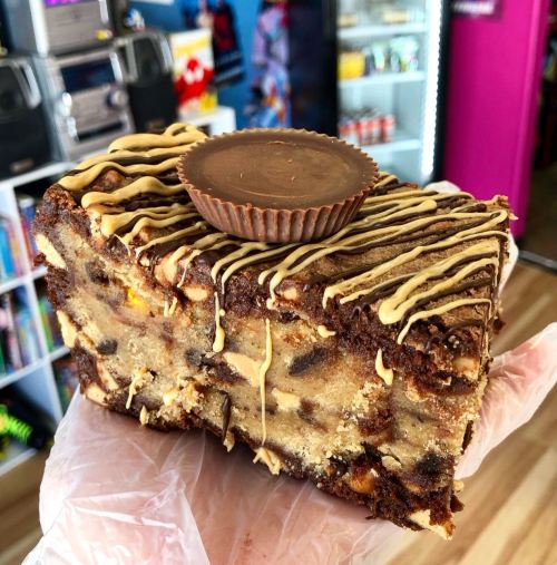 A hand holding a large brownie topped with a peanut butter cup and drizzled with chocolate and peanut butter.