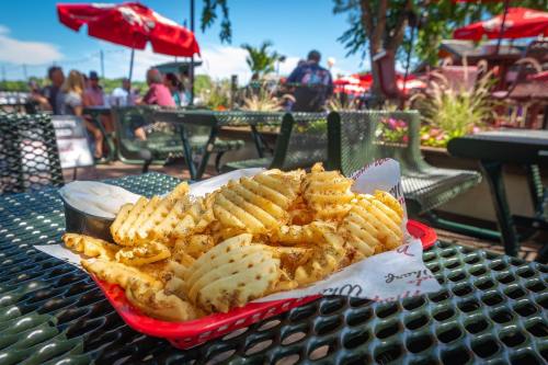 A basket of waffle fries with a dipping sauce, set on a table in a lively outdoor dining area.