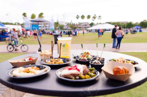A table with various dishes and a drink, set outdoors at a lively event with people and tents in the background.