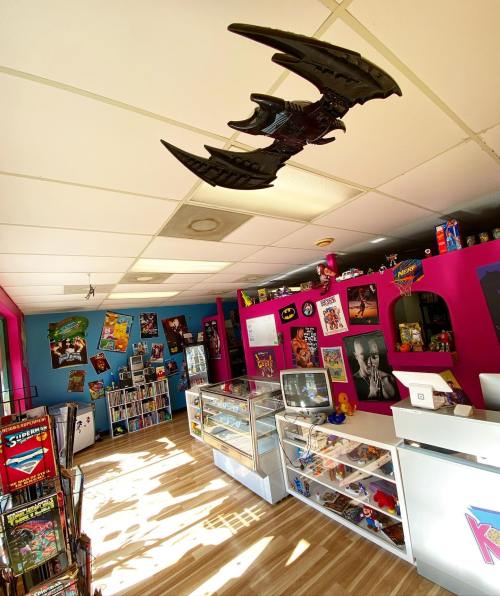 A colorful retro shop interior with collectibles, posters, and a bat-themed ceiling decoration.