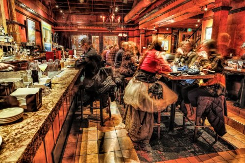 A bustling bar scene with patrons enjoying drinks, blurred motion, and warm, inviting decor.