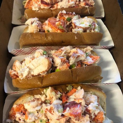 Four lobster rolls filled with chunks of lobster meat, served in soft, toasted buns.