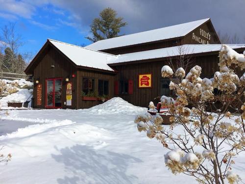 A cozy wooden building with red accents, surrounded by snow and trees, featuring a sign for Polly's Pancake Parlor.