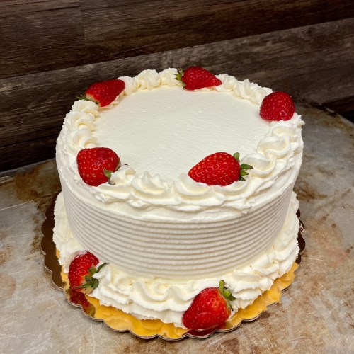 A round white cake decorated with whipped cream and fresh strawberries on top.