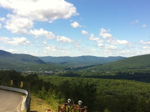 A scenic view of rolling green mountains under a blue sky with fluffy clouds, overlooking a valley.