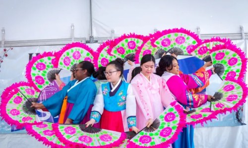 A group of dancers in colorful traditional attire perform with vibrant fans at a cultural event.