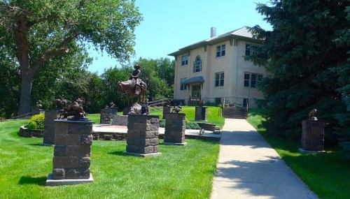 A pathway leads to a large building surrounded by sculptures and greenery on a sunny day.