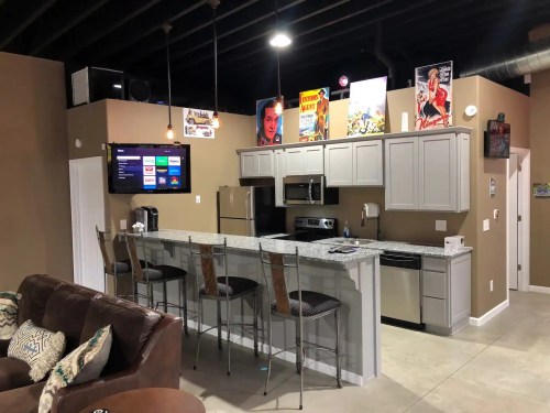 Modern kitchen with gray cabinets, granite countertops, bar stools, and retro posters on the walls.