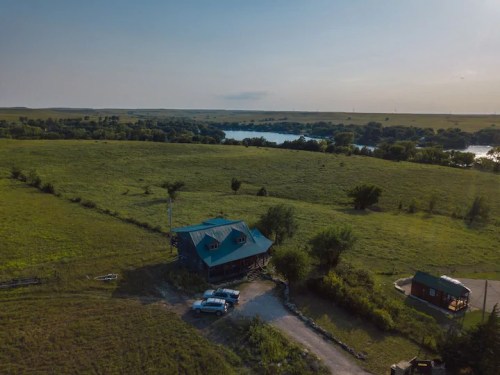 Aerial view of a blue-roofed house surrounded by green fields and a river in the background.