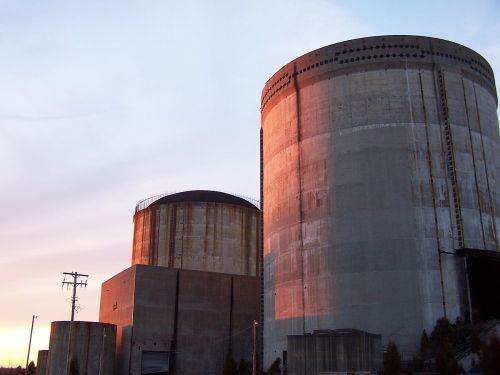 Two large, cylindrical concrete structures of a power plant, illuminated by sunset, against a colorful sky.