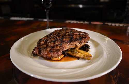 A perfectly grilled steak served on a white plate with roasted vegetables and a glass of red wine in the background.