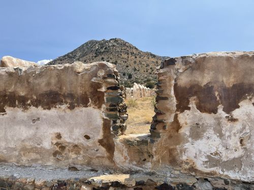 A view through a crumbling wall, with a mountain in the background under a clear blue sky.