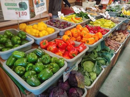 A vibrant display of various vegetables, including peppers, eggplants, and leafy greens, at a market stall.