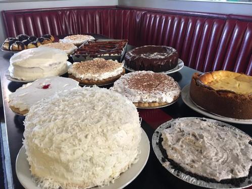 A variety of cakes and desserts displayed on a table, including chocolate, coconut, and cream pies.