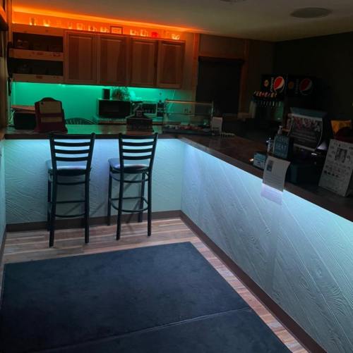A cozy bar area with illuminated countertops, two black chairs, and colorful lighting in the background.