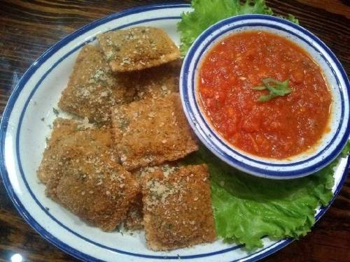 A plate of golden-brown fried ravioli served with marinara sauce and a bed of lettuce.