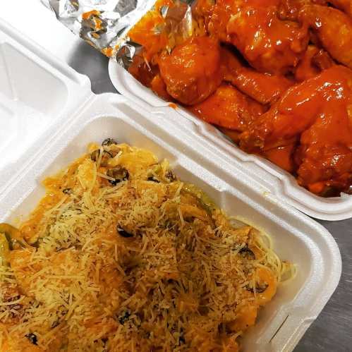 A takeout container with pasta topped with cheese and a side of spicy chicken wings.