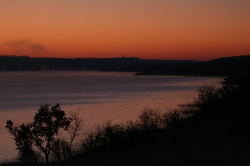 A serene lake at sunset, with silhouettes of trees and a colorful sky reflecting on the water's surface.