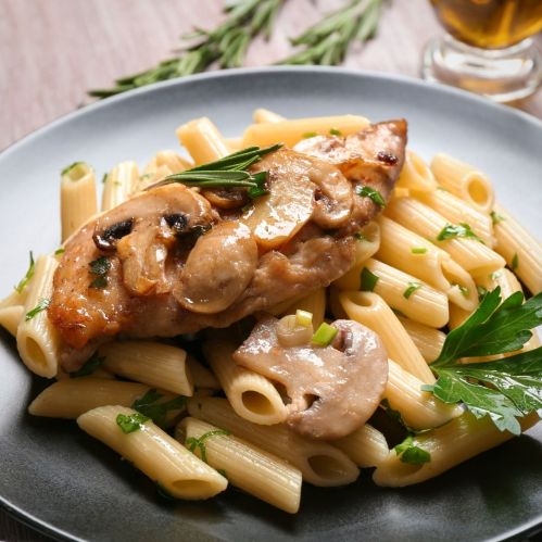 A plate of pasta topped with chicken, mushrooms, and herbs, garnished with parsley.