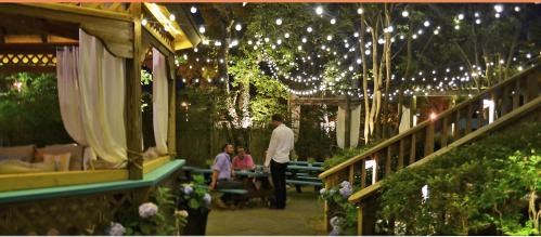 A cozy outdoor space with string lights, featuring seating areas and people enjoying the ambiance at night.