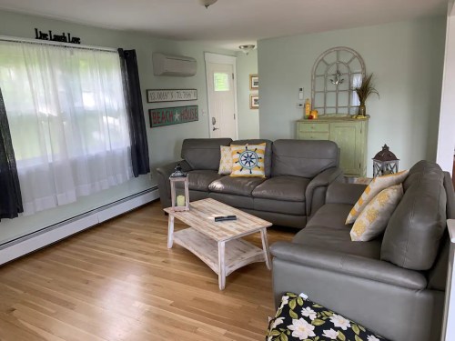 Cozy living room with light green walls, two sofas, decorative pillows, and a coffee table, featuring beach-themed decor.