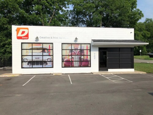A modern building with large windows displaying vintage cars, labeled "Dodo Creative & Print Services."
