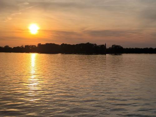 A serene sunset over a calm lake, with golden reflections on the water and silhouettes of trees in the background.