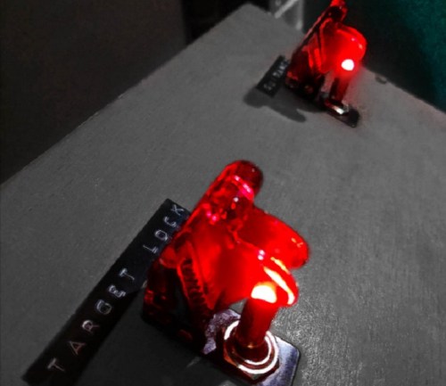 Two red toggle switches labeled "TARGET LOCK" illuminated on a gray surface.