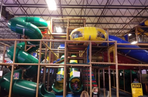 Colorful indoor playground with slides, climbing structures, and children playing.