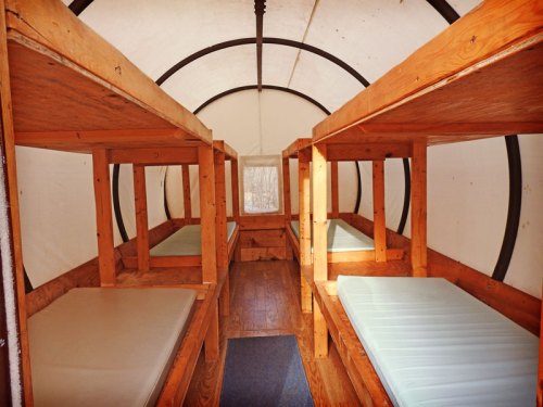 Interior of a rustic cabin with wooden bunk beds and a window, featuring a simple, cozy design.