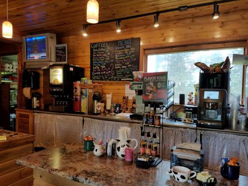Cozy café interior with a coffee station, menu board, and a view through large windows. Warm wooden decor.