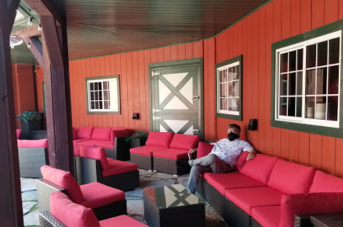 A cozy outdoor seating area with red couches and a man sitting quietly, surrounded by wooden walls and windows.