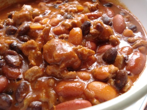 A close-up of a hearty chili dish with various beans and ground meat in a rich, thick sauce.