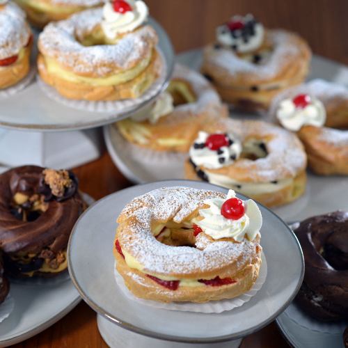 A variety of decorated pastries on plates, featuring cream, cherries, and powdered sugar.