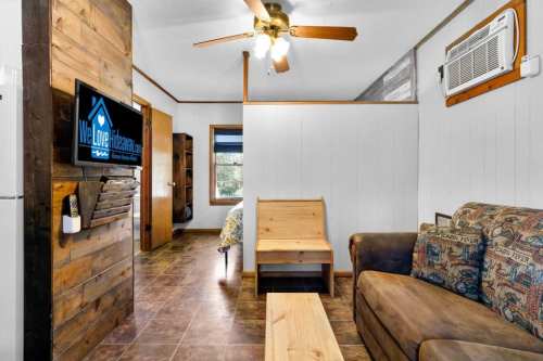 Cozy interior of a cabin featuring a sofa, wooden furniture, TV, and a ceiling fan. Bright and inviting atmosphere.