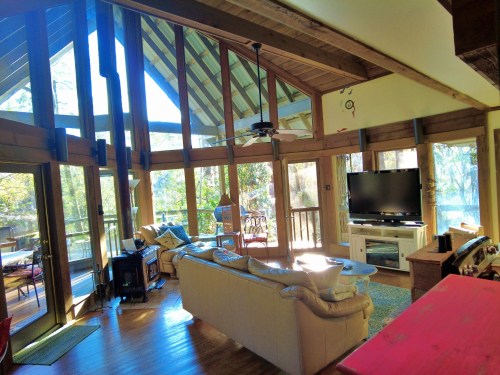 Bright, spacious living room with large windows, wooden beams, and a cozy seating area overlooking a scenic view.