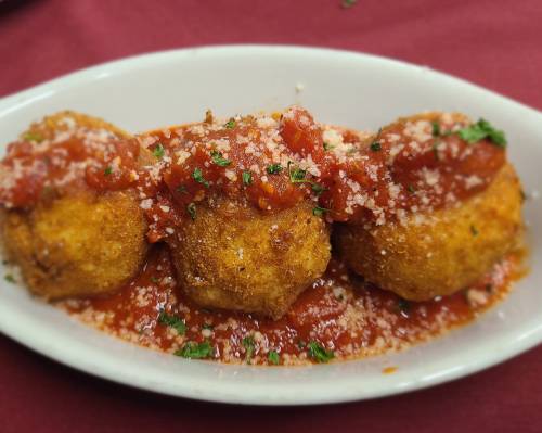 Three golden-brown fried balls topped with marinara sauce and grated cheese, served in a white dish on a red tablecloth.