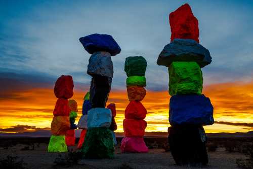 Colorful stacked boulders in various hues against a vibrant sunset sky in a desert landscape.