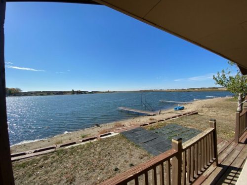 A serene view of a lake from a wooden deck, with clear blue skies and a small dock in the distance.