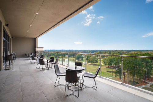 A spacious balcony with tables and chairs overlooking a green landscape and blue sky.